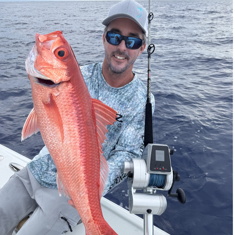 Man on a boat holding a large red fish with fishing equipment in the background.