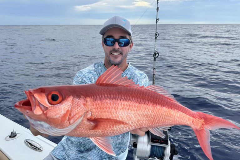Man holding a large red fish on a boat with ocean and sky in the background