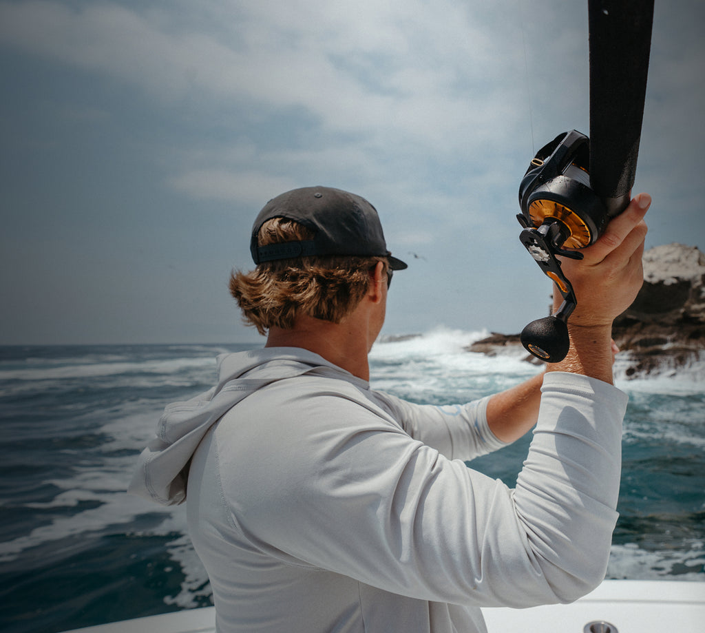 Man on a boat holding a fishing rod with a scenic ocean view