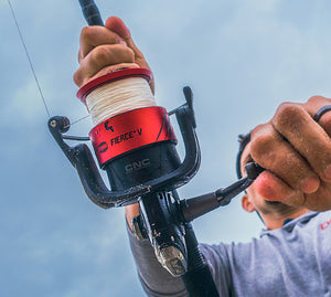 A close-up action shot of a person holding a spinning fishing rod with a red and black CNC Fierce V reel, set against a blue sky background.