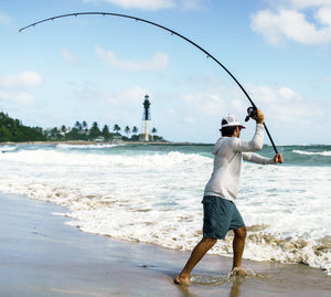 Man fishing on a beach with a lighthouse in the background