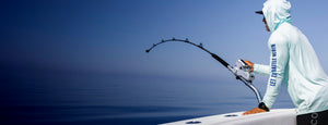 Person in a white raincoat fishing on a boat with a clear blue sky and ocean background